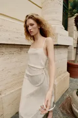 Vestido midi lencero de color blanco, confeccionado en tejido con efecto arrugado. Cuenta con escote recto, tirantes finos ajustables, diseño cruzado con cinturón fino para anudar y detalles de encaje en los acabados de la falda.