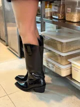 Botas tejanas altas de cuero charol color negro, con punta fina y diseño de caña alta con tiradores laterales.