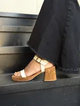 Sandalias de cuero color crudo, con dos tiras anchas sobre el empeine, pulsera al tobillo con hebilla y taco cuadrado de madera.