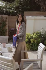 Chaqueta de punto color gris, con cuello pico y manga larga. Presenta un diseño de rombos (argyle) en tonos beige y negro en el frente. Cierre frontal con botones oscuros.