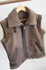 Chaleco estilo bomber de cuero negro con interior y detalles de piel sintética en color crema. Presenta cierre frontal con solapa de cuero en tono tostado y mangas de tejido de punto color crema.
