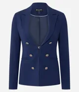 Blazer cruzado de sastrería en color azul marino, con corte slim y estructura entallada. Presenta solapas de muesca, cierre frontal con seis botones dorados metálicos con relieve, bolsillos con solapa en los laterales y mangas largas.