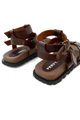 Sandalias de cuero marrón con tiras horizontales y ajuste con hebilla al tobillo.