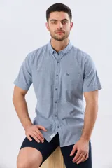 Camisa de manga corta confeccionada en mezcla de lino y algodón, con estampado de cuadros pequeños en tonos azules. Presenta cuello camisero con botones, cierre frontal abotonado, bolsillo aplicado en el pecho y dobladillo redondeado.