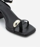 Sandalias negras de tacón ancho, con tiras finas, puntera cuadrada, adorno metálico dorado en el dedo gordo, cierre con hebilla en el tobillo y tacón mediano.