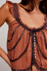 Musculosa blanca de poliéster con diseño romántico, tirantes con volados, detalles de encaje y cierre frontal con cordón ajustable y botones.