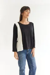 Remera de manga larga con diseño bicolor, combinando cuerpo negro con una franja lateral en color crudo. Presenta cuello redondo, pespuntes a contratono y un corte asimétrico con tajos laterales, siendo más corta en la parte delantera.