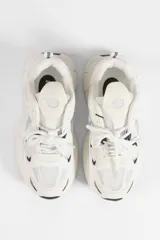 Zapatillas urbanas de suela alta, con diseño multicapa que combina malla y paneles sintéticos en tonos blanco y crema, con pequeños detalles en negro.