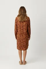 Vestido camisero de manga larga, color marrón con estampado abstracto en tonos más claros. Tiene cuello de camisa y cierre frontal con botones blancos.