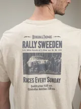 Remera blanca de algodón con estampado gráfico en la espalda en color rojo. El estampado incluye el texto "Benson & Thomas Rally Sweeden", una imagen de un auto de rally clásico y detalles de horarios de carreras.