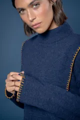 Buzo de lana color beige con cuello redondo y mangas largas. Presenta costuras decorativas con bordado en color naranja a lo largo de los costados y en los puños.