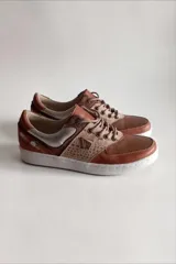 Sneakers de cuero marrón con detalles en cobre, paneles texturizados, talón plateado y suela blanca.