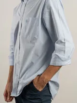Camisa de corte regular confeccionada en tejido Oxford de algodón. Presenta un diseño de rayas verticales en tonos azul y blanco, con cuello abotonado, bolsillo frontal en el pecho con logo bordado y mangas largas con puños ajustables.