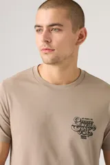 Remera de manga corta color beige, con cuello redondo y un pequeño estampado gráfico en el pecho.