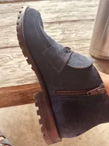 Botín de gamuza azul marino con cierre lateral y hebilla metálica decorativa.