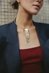 Gargantilla rígida dorada con dije rectangular irregular con textura de arena.