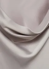 Vestido corto de satén color gris claro, con cuello drapeado y manga larga. Presenta un diseño recto y fluido.
