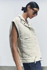 Chaleco gris acolchado con cuello alto, cierre frontal con cremallera metálica, bolsillos de plastrón en delantero y bajo ajustable con cordones.