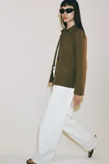 Chaqueta de estilo utilitario color verde militar, con cuello solapa, manga larga y cierre frontal con botones ocultos por solapa. Presenta bolsillos con solapa en la parte delantera y un bolsillo de plastrón en el pecho.