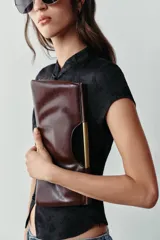 Bolso de mano de diseño estructurado en color bordó, con asa rígida dorada integrada en la parte superior y cierre magnético.