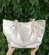 Bolso tipo tote de cuero color plateado con acabado metalizado. Tiene doble asa de hombro con detalle de nudo.