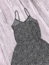 Mono corto de color negro con estampado de pequeñas flores blancas, breteles finos, escote en V y botones decorativos en el frente. Presenta una cintura elástica que define la silueta y shorts sueltos.