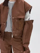 Campera de denim a rayas verticales con cuello de pana en color bordó. Presenta cierre frontal, mangas desmontables con cierre en los hombros, canesú en el pecho y bolsillos de parche cuadrados.