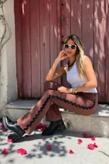 Pantalon de gabardina elastizada color marron chocolate, de corte recto y tiro medio. Presenta una guarda decorativa de cinta negra con borde ondulado a lo largo de las costuras laterales.