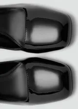 Zapato de tacón cuadrado en charol negro, con punta cuadrada y tira ajustable al tobillo con hebilla.