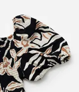 Blusa de crepé con estampado floral en tonos beige y negro, escote recto y mangas cortas abullonadas con puños elásticos.