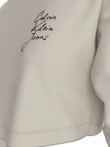 Remera cropped color beige de algodón, con cuello redondo y mangas largas. Presenta el logo de Calvin Klein Jeans estampado en el pecho.