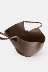 Bolso de hombro estilo capazo, color marrón, con doble asa de hombro y cuerpo con pespuntes. Presenta un cierre mediante pasador con clip metálico y una bolsa interior extraíble con cierre fruncido.