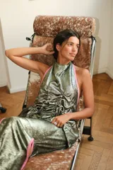 Top de escote halter confeccionado en tejido metalizado color verde con vivos rosados en lino. Presenta jaretas frontales que crean un efecto fruncido con volumen, espalda descubierta y ajuste mediante tiras para anudar.