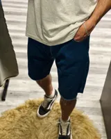 Short de jean de mezclilla azul oscuro, corte ancho y largo (tipo bermuda), con bordes deshilachados y dobladillo sin rematar.