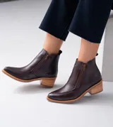 Bota corta de cuero vacuno color negro, con diseño combinado de cuero liso y cuero con textura de reptil en el empeine. Presenta punta fina, taco cuadrado de 6 cm y doble cierre lateral.