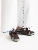 Zapatillas de cuero vacuno en color beige, con recortes de gamuza en la puntera y talón, doble cordón en tonos gris y marrón, hebilla lateral y dije colgante en la cordonera. Suela plana de goma.