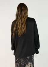 Blusa de satén color blanco con escote en V, cuello con volados y mangas largas con puños también decorados con volados.