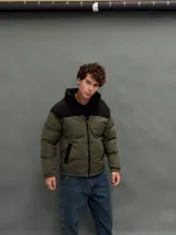 Campera puffer con capucha, diseño bicolor en verde oliva y negro, cierre frontal y bolsillos laterales.