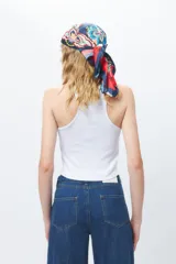 Top de algodón blanco sin mangas con cuello halter y bajo asimétrico en punta diagonal. Presenta un tejido de punto acanalado y un diseño inspirado en la estética de los años 2000.