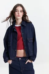 Campera de jean de mezclilla oscura, corte relajado, con cuello y bolsillos de parche con tapa y botón en el pecho. Presenta costuras en tono naranja/marrón claro.