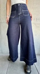 Pantalón de jean azul oscuro, de corte ancho, con bolsillos delanteros cuadrados y costuras blancas contrastantes.