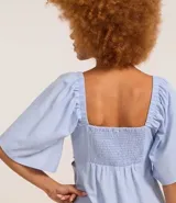 Vestido corto evasé color celeste, con escote en V, mangas cortas amplias, recorte cutout en los laterales de la cintura y volado en el bajo.