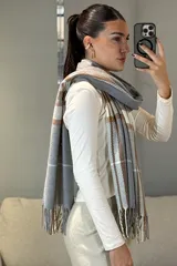 Bufanda rectangular de tejido suave con diseño de cuadros escoceses en tonos mostaza, blanco y gris, terminada con flecos en los extremos.