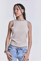 Musculosa color crudo de punto canalé, con cuello redondo y sisas con apliques de tachas plateadas.