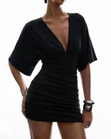 Minivestido negro de escote en V profundo, mangas amplias estilo murciélago y diseño ajustado con efecto drapeado. Cuenta con espalda semi descubierta y detalle de lazo para anudar.
