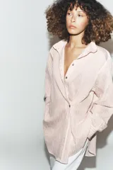 Camisa de corte oversize con estampado de rayas verticales, cuello subido y cierre frontal con botones. Presenta mangas largas con puños y un diseño cruzado en la parte delantera.