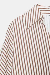 Camisa de corte holgado confeccionada en mezcla de lino, con estampado de rayas verticales en color marrón y blanco. Presenta cuello solapa, escote en pico, cierre frontal con botones y mangas amplias por debajo del codo con puños definidos.
