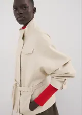 Chaqueta beige de cuello alto, manga larga con puños abotonados, bolsillo con solapa en el pecho, cinturón ajustable para la cintura y cierre frontal de cremallera oculta.