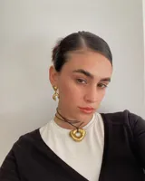 Collar con dije de forma irregular en tonos dorados y plateados, suspendido de un cordón doble de algodón negro.