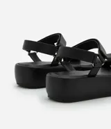 Sandalia flatform negra de material sintético, con punta redonda y tiras torcidas.